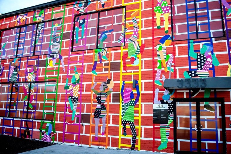 Lift As You Climb is a vibrant mural by Derrick Adams that depicts eye-catching figures helping each other climb colorful ladders to the top of the building that houses Sophie's Artist Lounge.